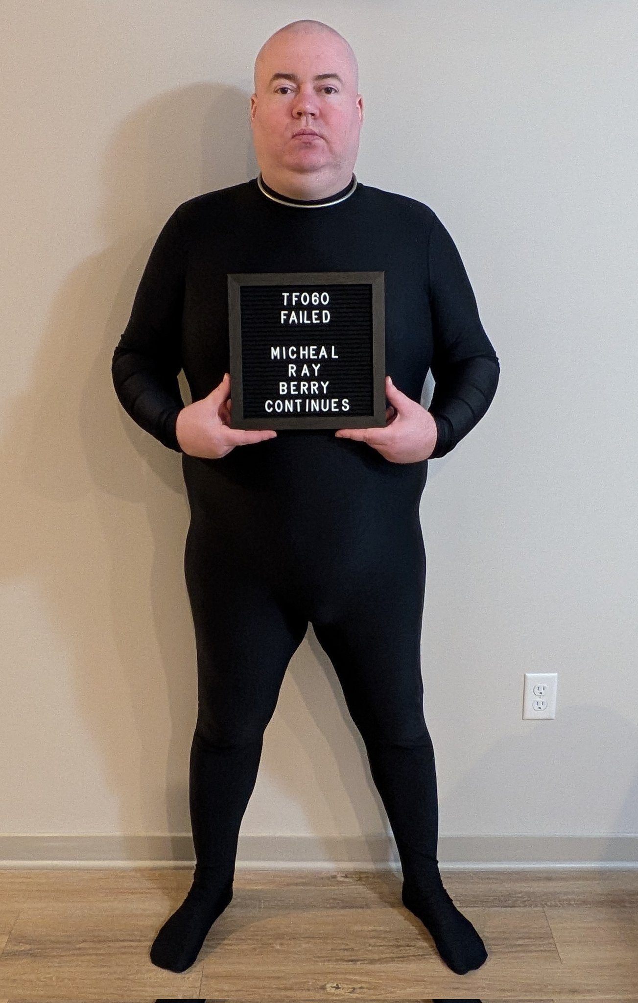 Micheal Ray Berry standing in the black project uniform, holding a sign that reads “TF060 failed. Micheal Ray Berry continues.”